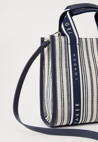 Sac fourre-tout rayé aux couleurs bleu marine et crème, avec un tissu texturé, des poignées robustes et une bandoulière en cuir détachable.