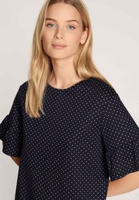 Navy blue top made of smooth fabric, featuring white and pink polka dots, short ruffled sleeves, and a round neckline.