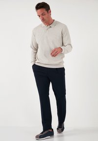 Polo shirt bej, cu mânecă lungă, cu dungi, având guler, asortat cu pantaloni drepti de culoare albastru închis și adidași eleganți gri și albastru.