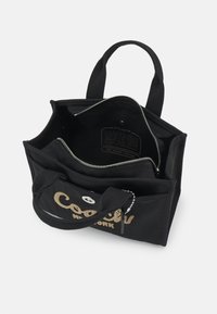 Sac à main Coach noir avec doubles poignées, poche avant à pression et compartiment principal ouvert avec poche zippée à l'intérieur, marqué "Coach New York" à l'avant.