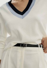 Gräddvit stickad tröja med en svart och ljusblå v-ringning, matchad med högmidjade krämfärgade byxor, som förstärks av ett svart bälte.