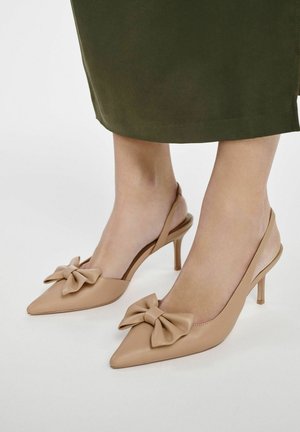 Beżowe szpilki typu slingback z wyostrzonym noskiem i dużą kokardą z przodu. Obcas jest smukły i ma około 7 cm wysokości.