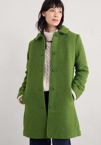 Grön ullblandad kappa med knappstängning, krage och texturerad yta. Har sidfickor och en avslappnad passform.