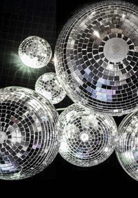 Cinq boules disco, composées de petits carreaux de miroir réfléchissants, de forme ronde, suspendues sur un fond noir, reflétant la lumière.