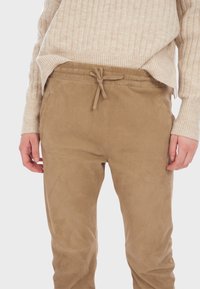 Tan joggerbroek van zacht suede-achtig materiaal, met een trekkoord taille, zijzakken en een gladde textuur.