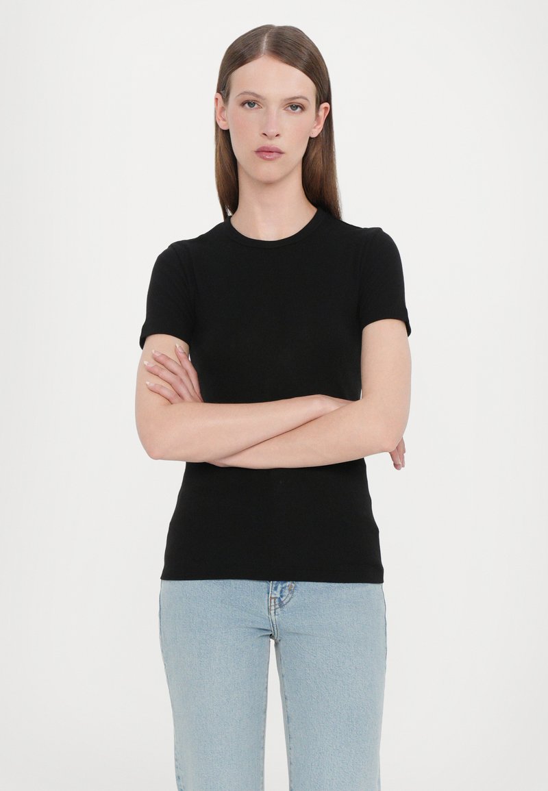Top nero a maniche corte con scollo rotondo, realizzato in un tessuto liscio, abbinato a jeans chiari a vita alta. Design semplice.