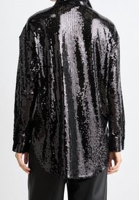 Black sequin shirt with a loose fit, long sleeves, and a high collar. The sequins create a shimmering effect with alternating shiny and matte finishes.