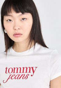Balta medvilnė t-shirt, su raudonu logotipu "tommy jeans" kursyvu. Trumpomis rankovėmis, klasikinio kirpimo, lygi tekstūra.