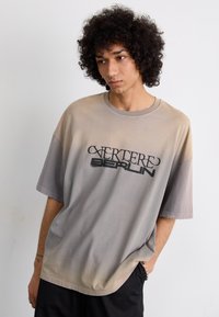 Oversized short-sleeve T-shirt in gradient gray with black "Vertere Berlin" text; soft cotton fabric, relaxed fit, minimal stitching details.