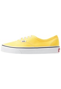 Žluté plátěné tenisky s bílými tkaničkami a gumovou podešví. Mají černý lem podél podešve a malé logo Vans na boku.