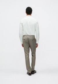 Camicia bianca a maniche lunghe abbinata a pantaloni eleganti grigio chiaro con motivo a quadri, dotati di tasche posteriori e scarpe scure, vista da dietro.
