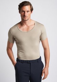 Beige, short-sleeve fitted T-shirt with a V-neck design, made from smooth material, worn over dark trousers, highlighting a slim profile.