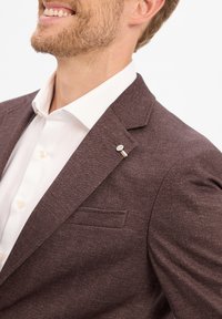 Burgunderfarbener Blazer aus strukturiertem Stoff, mit Reverskragen, einer einzelnen Brusttasche und einer silbernen Akzentnadel am Kragen, kombiniert mit einem weißen Hemd.