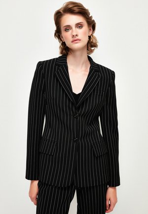 Black pinstriped blazer with a structured design, featuring a peaked lapel, two front pockets, and buttons for closure.
