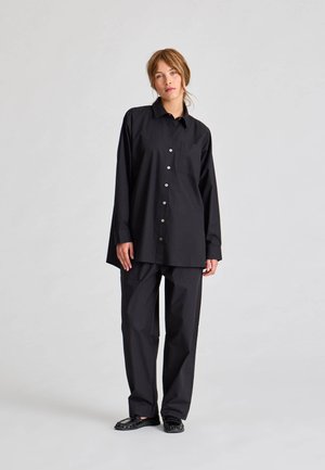 Fekete, hosszú ujjú, gombos ing, bal oldalon zsebbe, laza fekete nadrággal párosítva, mindkettő sima anyagból készült.