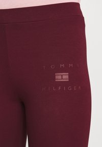 Leggings burdeos hechos de un material suave y elástico presentan un sutil logotipo tonal de "TOMMY HILFIGER" cerca de la cintura.