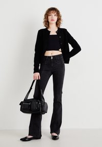 Črn cardigan z zadrgo, skrajšan top, črne široke jeans hlače z zapiranjem na dva gumba ter črna sijoča torbica. Ravne črne čevlje.