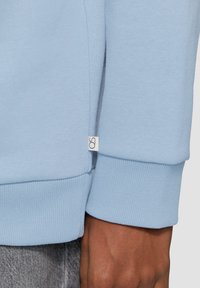 Lichtblauwe sweatshirt met ribgebreide manchetten, een zijsplits en een klein logo-label nabij de zoom. Zacht, getextureerd stof.