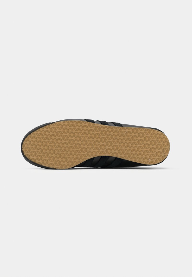 Black athletic shoe sole with a textured, honeycomb rubber grip pattern. Features a smooth black upper and three black stripes along the sides.