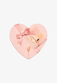 Scatola regalo a forma di cuore in un morbido rosa, con una texture trapuntata, nastro di raso e etichetta con marchio. Contiene prodotti di bellezza all'interno.