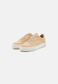 Beige suede sneakers with a rounded toe, lace-up design, and white rubber sole. Features minimal branding and textured surface.