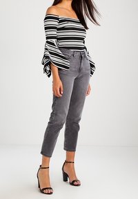 Top off-the-shoulder con righe bianche e nere e maniche a campana; abbinato a jeans grigi a vita alta e tacchi neri con cinturini.