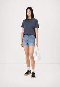 Dark gray short-sleeve t-shirt paired with light blue denim shorts. Black sneakers with white accents and a small white handbag.