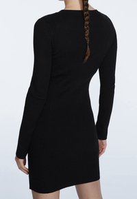 Robe noire à manches longues côtelées avec une coupe ajustée, longueur genoux et encolure ronde. Texture lisse avec un subtil motif vertical.
