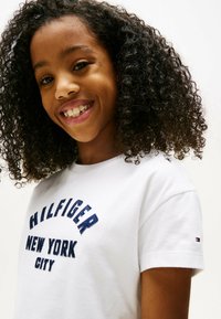 T-shirt bianco in cotone con testo ricamato blu navy "HILFIGER NEW YORK CITY", maniche corte e un piccolo logo sulla manica sinistra.
