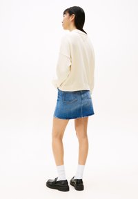 Kremfarget genser med senkede skuldre og ribbestrikket kant, kombinert med et denim miniskjørt. Modellen har på seg hvite sokker og svarte sko.