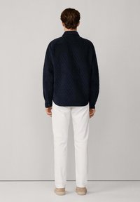 Granatowa pikowana koszula z kołnierzykiem, długimi rękawami i prostym krojem, w połączeniu z białymi spodniami i beżowymi butami.