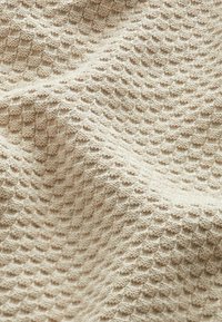 Beigen värinen, teksturoitu kangas, jossa on mehiläiskenno-kuvio, kohokuvioituja neliöitä ja pehmeä, kudottu ulkonäkö. Sopii monenlaisiin tekstiilisovelluksiin.