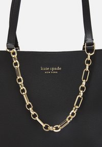Czarna skórzana torba tote o teksturowym wykończeniu, z dodatkiem złotego łańcuszka oraz nazwą marki "kate spade" w złotych literach.