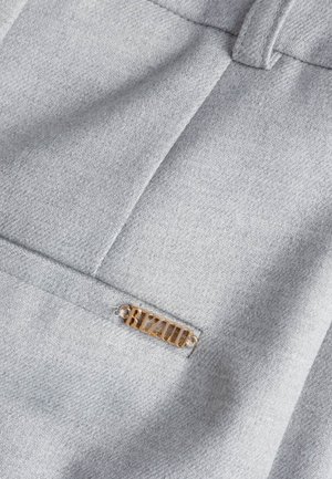 Zbliżenie na szare ubranie z tkaniny z małą poziomą kieszenią i przymocowaną złotą metką z logo "BIZUU".