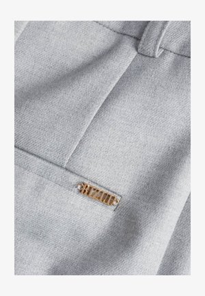 Zbliżenie na szare ubranie z tkaniny z małą poziomą kieszenią i przymocowaną złotą metką z logo "BIZUU".