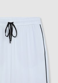 Shorts atletici bianchi con cordino nero, dotati di vita elasticizzata e piping laterale nero. Tessuto leggero con una superficie liscia.