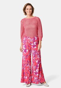 Pull en tricot rose à manches longues associé à un pantalon floral à jambes larges dans des teintes vives de rose et de violet, avec une coupe décontractée et une taille élastique.