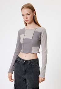Top grigio corto con maniche lunghe, caratterizzato da un design a patchwork di diverse trame e tonalità. Abbinato a pantaloni neri a vita alta.