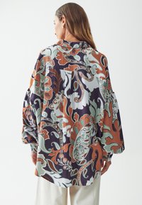 Camisa de manga larga con un patrón de paisley floral multicolor sobre un fondo claro. Fabricada con tela ligera y de corte holgado.