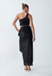 Black sequined two-piece outfit featuring a one-shoulder top and a high-slit skirt, paired with nude heels. Smooth texture with shiny accents.