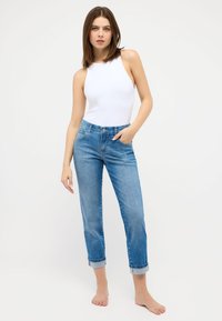 Weißer ärmelloser Bodysuit kombiniert mit hochgekrempelten hellblauen Jeans. Die Jeans haben fünf Taschen und einen lockeren Schnitt.
