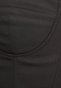 Čern�á látka s texturovaným povrchem, s křivkovým tvarem kapsy a viditelnými švy. Design je elegantní a minimalistický.