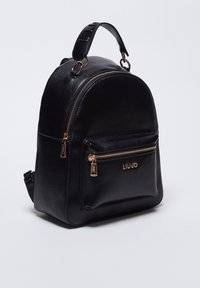 Sac à dos en cuir noir à forme arrondie, doté de ferrures dorées, d'une poche avant zippée et de bretelles ajustables. Logo embossé à l'avant.