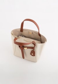 Beige lædertaske med brune læderhåndtag og en justerbar rem. Indeholder en lynlåslomme indeni og en hardware-detalje i guldtonet.