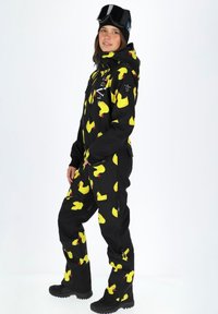 Zwarte winterjas bedekt met grote gele rubberen eendpatronen, met een rits aan de voorkant, verstelbare manchetten en stevige laarzen.