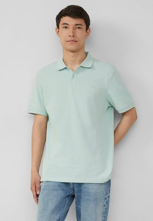 Hellgrünes Poloshirt mit klassischem Kragen, kurzen Ärmeln und feiner Textur. Trägt man mit hellblauen Jeans. Einfaches Logo auf der Brust.