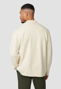 Crèmekleurige gebreide trui met een ontspannen pasvorm, lange mouwen, ribbeldetails aan de zoom en een kraag. De stof lijkt zacht en soepel.