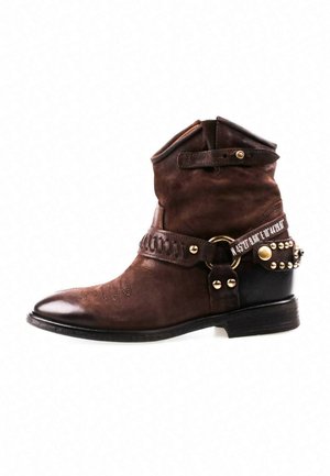 Bottine en cuir marron avec le dessus plié, des sangles décoratives, des clous en métal et une partie talon noire avec des accents dorés.