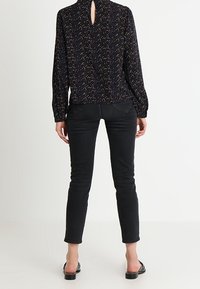 Blusa nera a manica lunga con dettaglio a chiave sul retro, caratterizzata da un motivo a macchie multicolori, abbinata a jeans neri aderenti e sandali piatti.