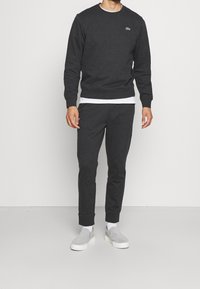 Mörkgrå sweatshirt och matchande joggers i mjukt material. Har rund halsringning, ribbade muddar och en liten logotyp på bröstet.